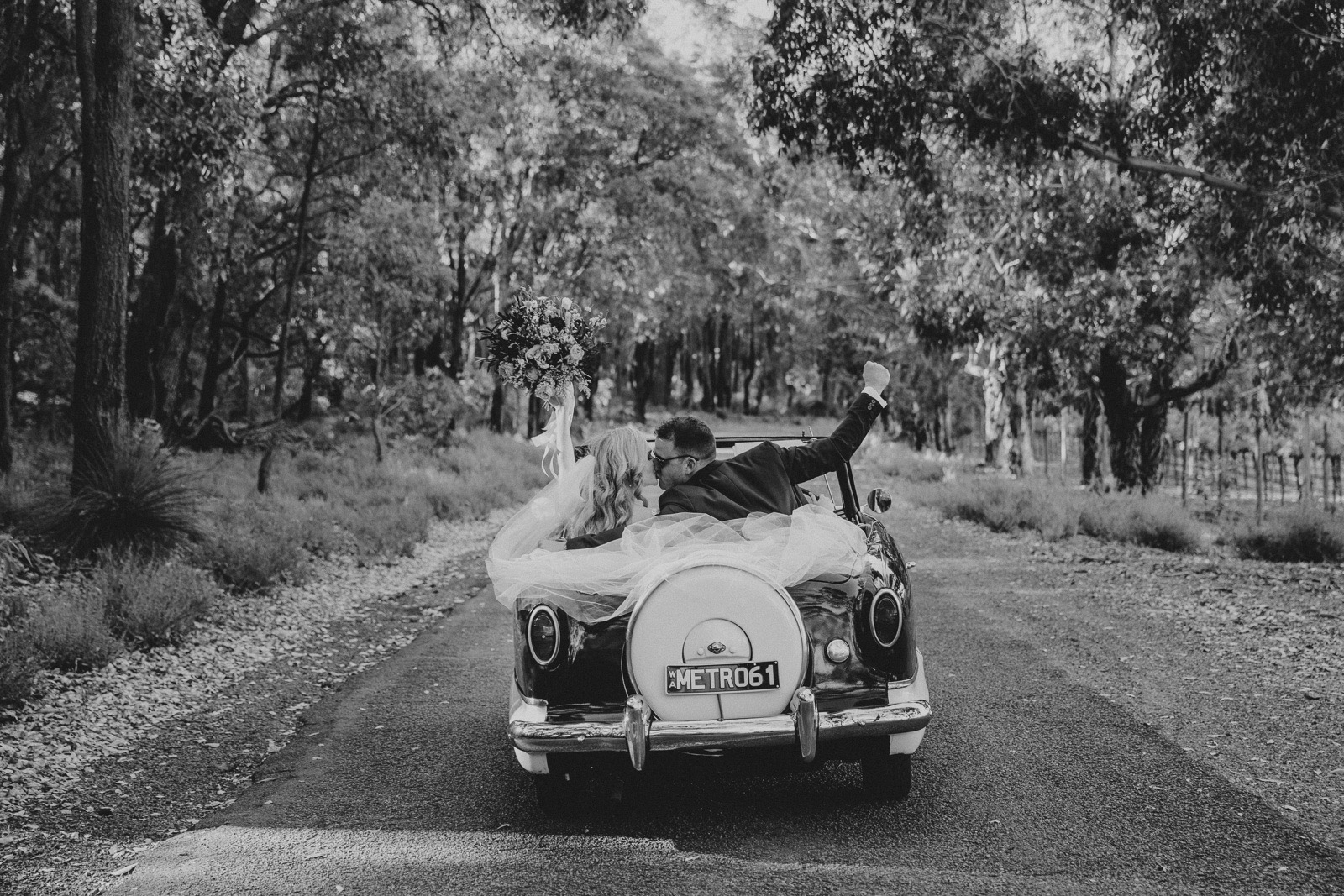 Bride and groom driving away in a vintage convertible